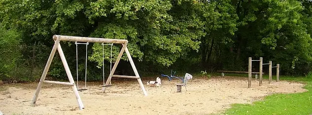 Spielplatz mit Schaukel für zwei Kinder, zwei Schaukeltiere, sandiger Boden, Sitzbank, Reck mit 3 verschiedenen Höhen 